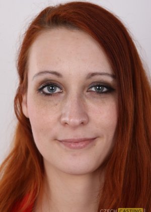 Любительская девушка с длинными рыжими волосами стоит прямо и узко, раздеваясь