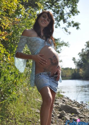 Pregnant girl Brianna strips to flat shoes on a riverbank in a serene setting